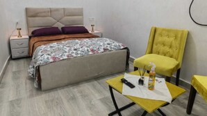 A bedroom with a bed, bedside tables, a chair, and a small table with a remote control and a bottle. - Mydar medina (Tanger)