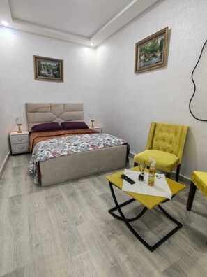 Ein Schlafzimmer mit einem Bett, Nachttischen, einem Sessel und einem kleinen Tisch mit Fernbedienung und Flasche.