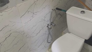A bathroom with a toilet, a shower, and a tiled wall with a marble pattern. - Mydar medina (Tanger)