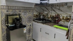 A compact kitchen with white cabinets, a stainless steel refrigerator, and patterned backsplash tiles. - Mydar medina (Tanger)
