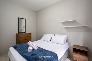 Ein Schlafzimmer mit einem Bett, einer Holzkommode, einem Nachttisch und einem an der Wand befestigten Regal.