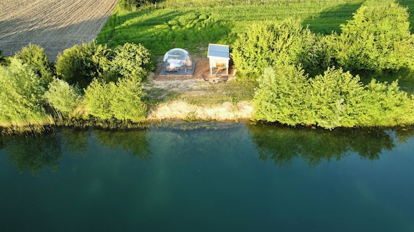 Vista aérea de una propiedad aislada junto al lago, con una estructura de cúpula transparente y una cabaña pequeña.