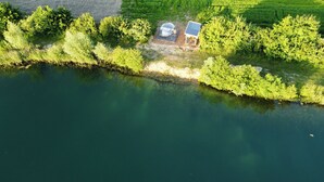 An aerial view of a lakeside property with a transparent dome structure, a small building with a sloped roof, and lush greenery surrounding the area. - The Most Beautiful Way | To Say | "I Love You" (Wadersloh)
