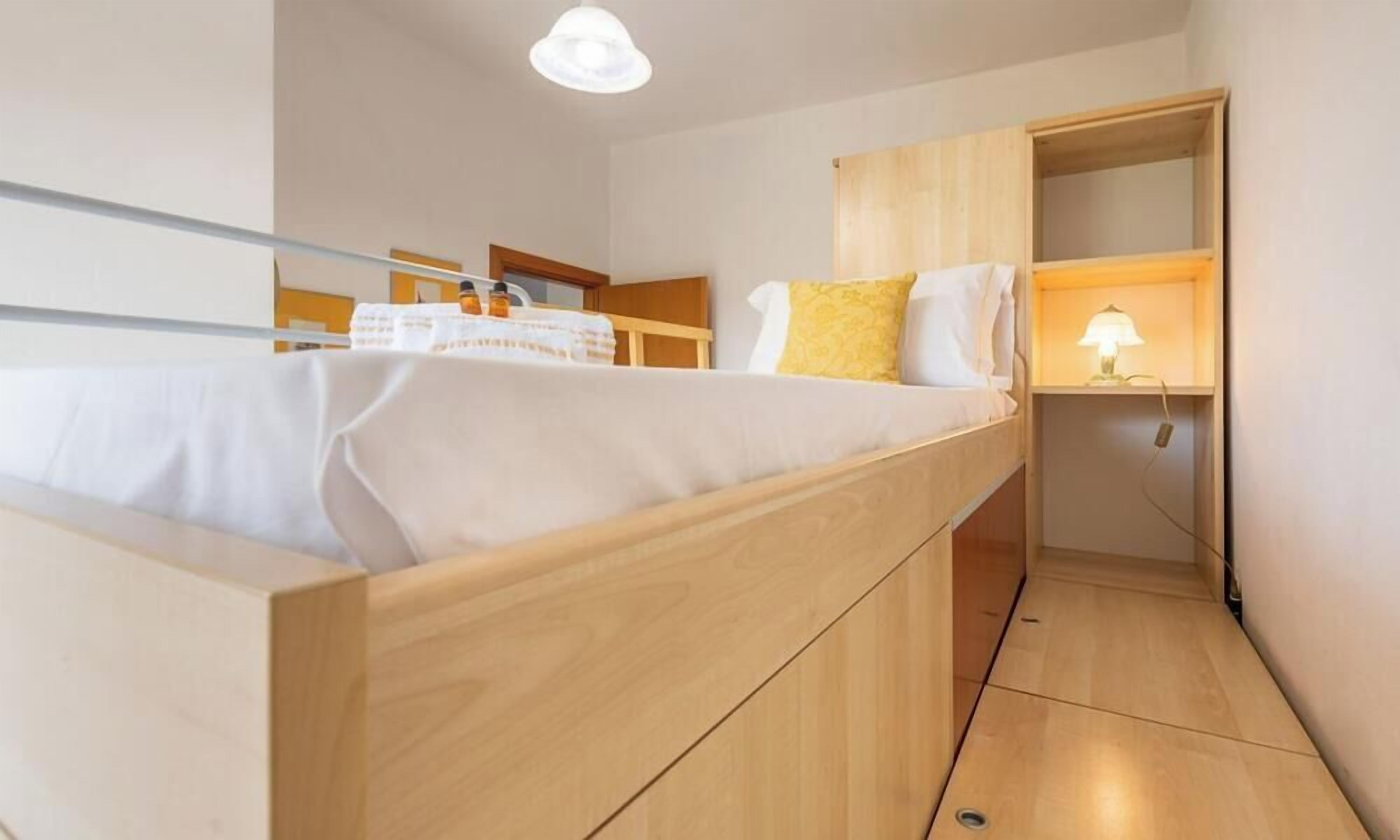 Una habitación pequeña con cama, un escritorio con lámpara y un armario de madera.