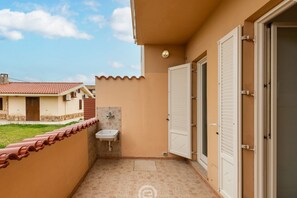 A balcony with a sink, a door, and a view of a building with a tiled roof.