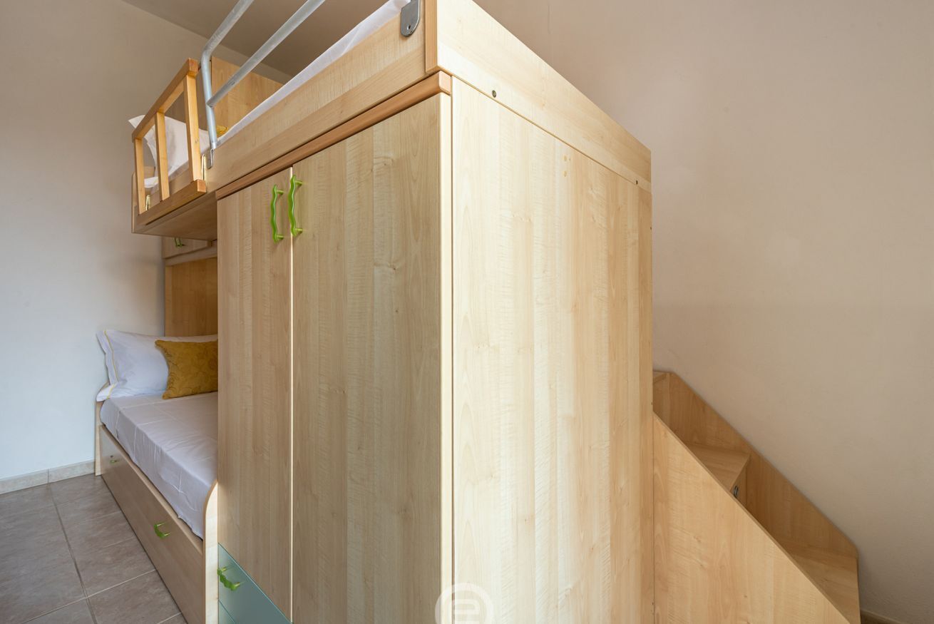 Een kamer met een stapelbed, een houten garderobe en een trap.