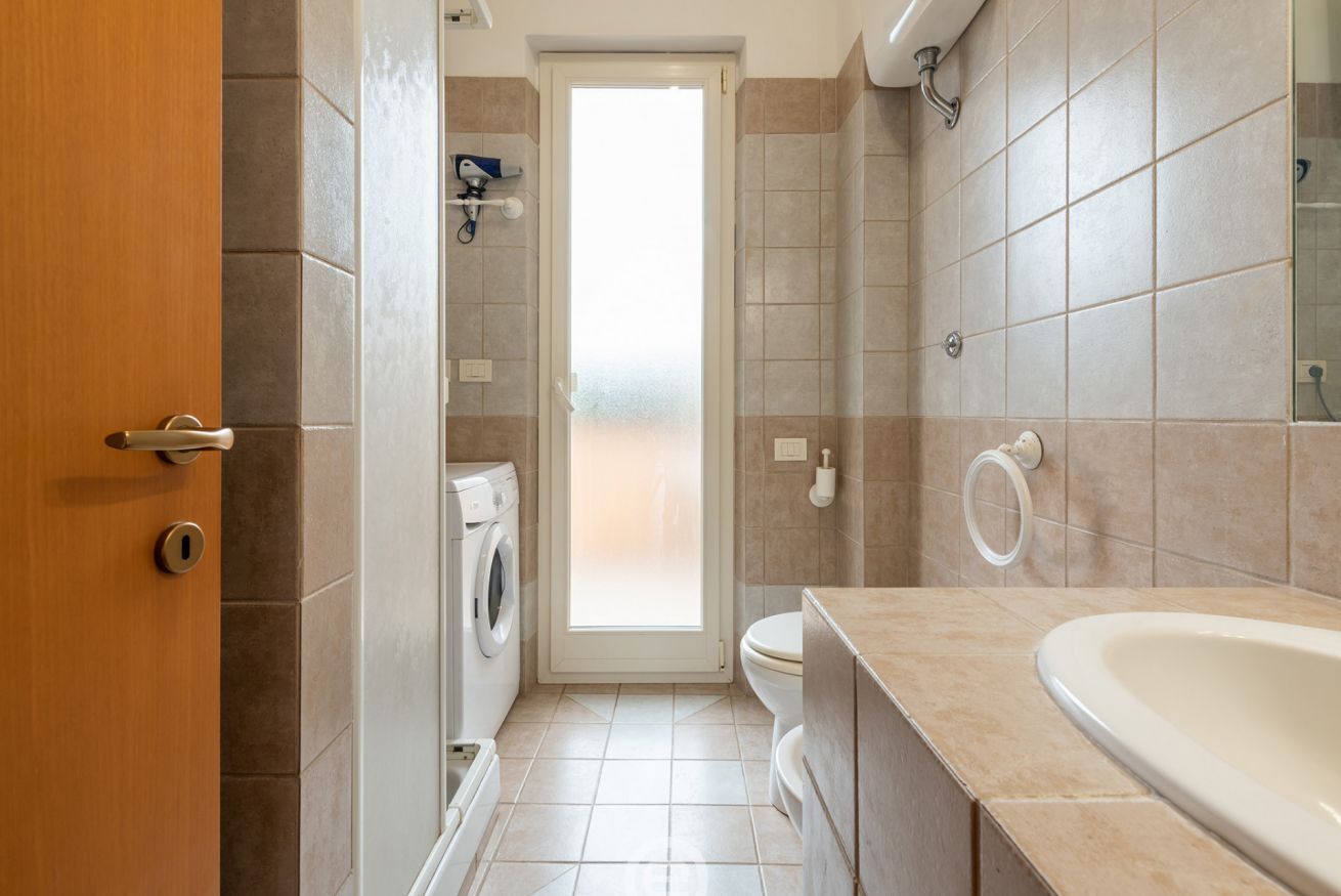 A compact bathroom with a washing machine, toilet, and a bathtub.