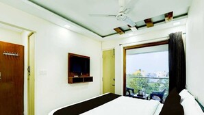 A hotel room with a bed, a television, a ceiling fan, and a window with a view. - Townhouse R S Puram Junction (Coimbatore)