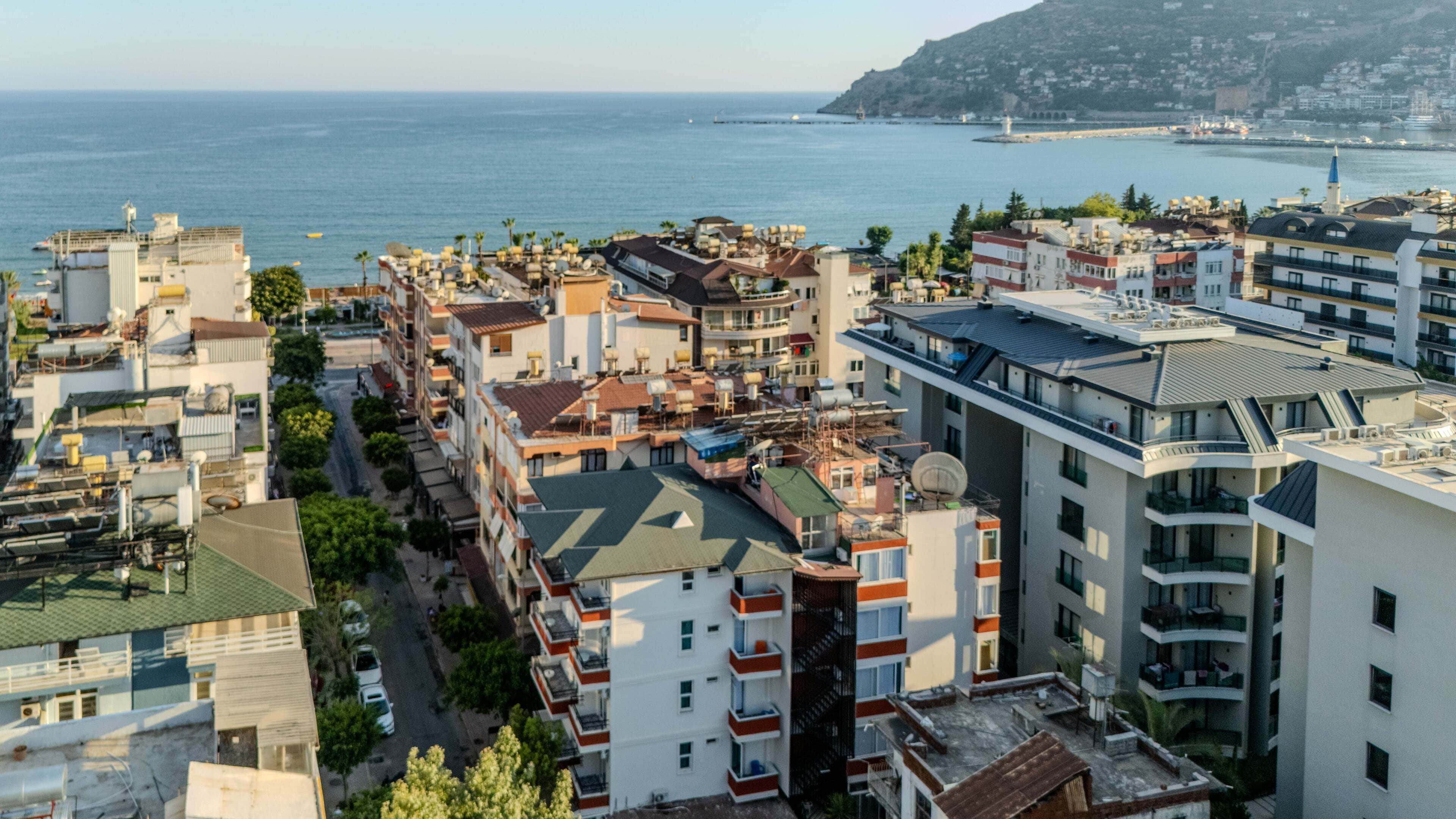 Un paysage urbain côtier, avec un mélange de bâtiments résidentiels, dont certains sont dotés de balcons et de terrasses, et un phare imposant qui se distingue à l’horizon.