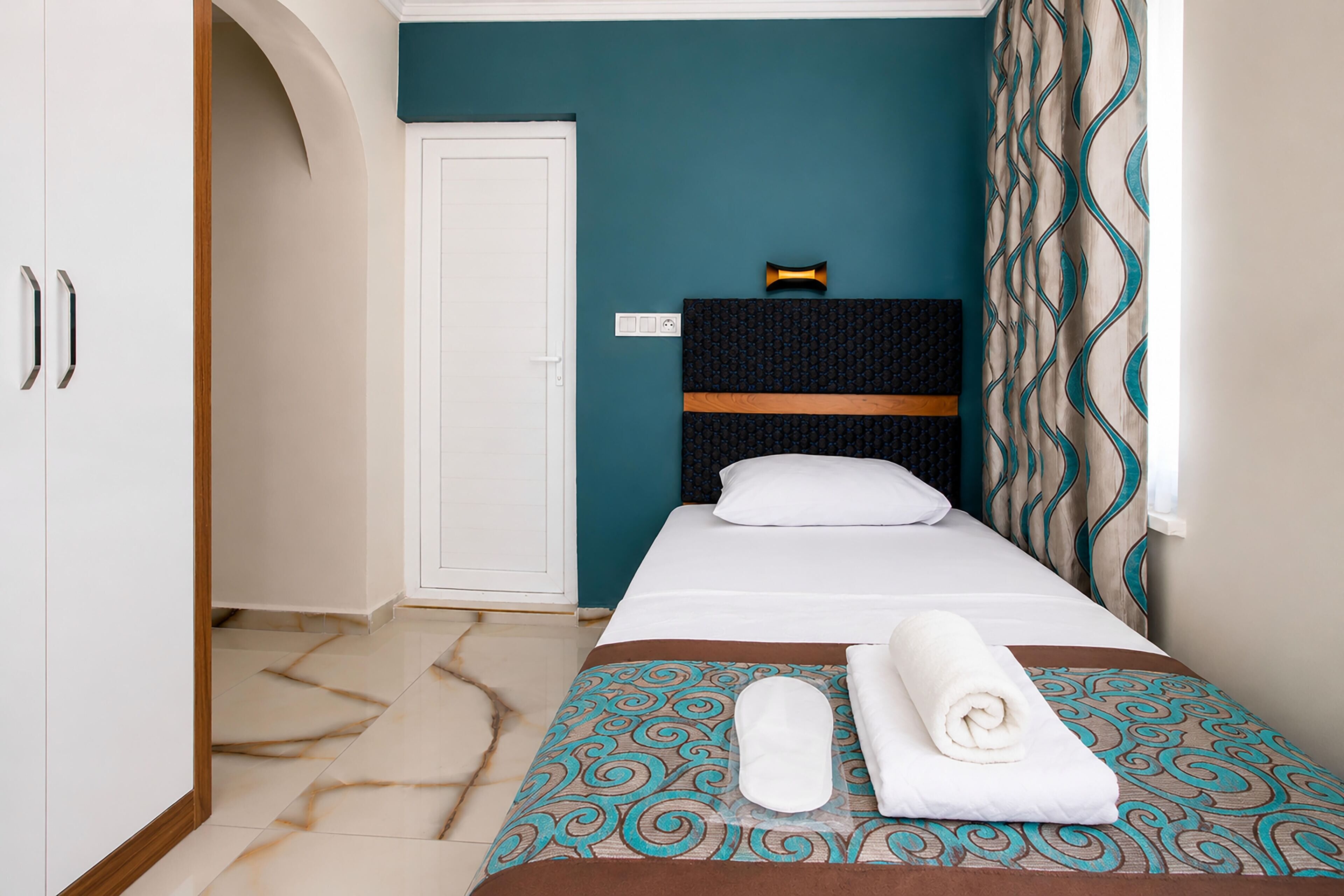A hotel room with a bed, a wardrobe, a door, and a wall-mounted light fixture.