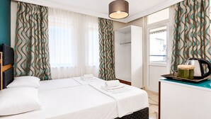 Et hotelværelse med seng, gardiner, et natbord med elkedel og udsigt gennem vinduet.