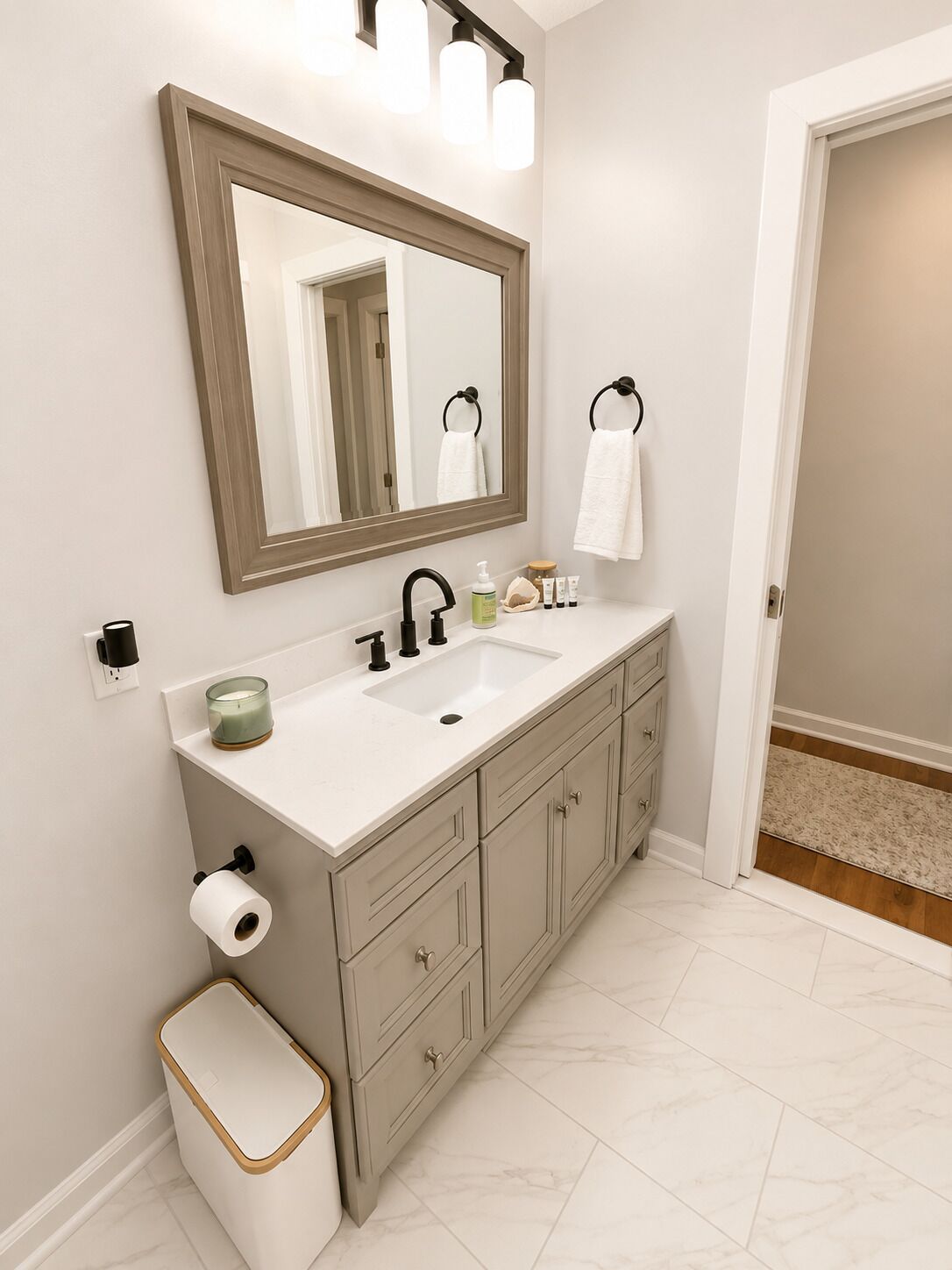 A bathroom with a large mirror, a sink, a toilet, and a trash can.