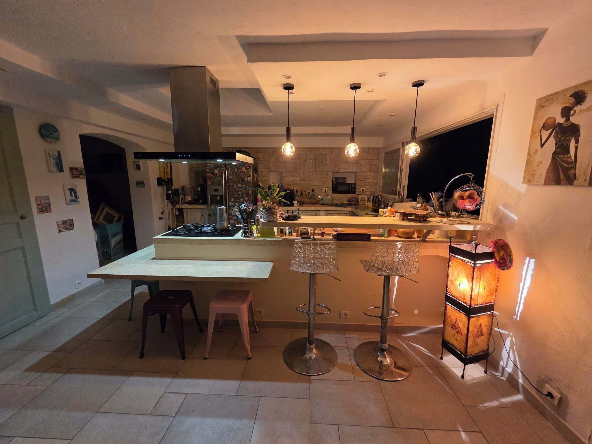 A modern kitchen with a central island, pendant lights, and a bar area.