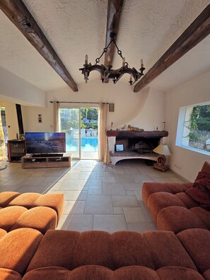A living room with a fireplace, a television, and a view of a pool through a glass door. - A tropical getaway in a private villa near the sea and Nice on the French Riviera! (La Gaude)