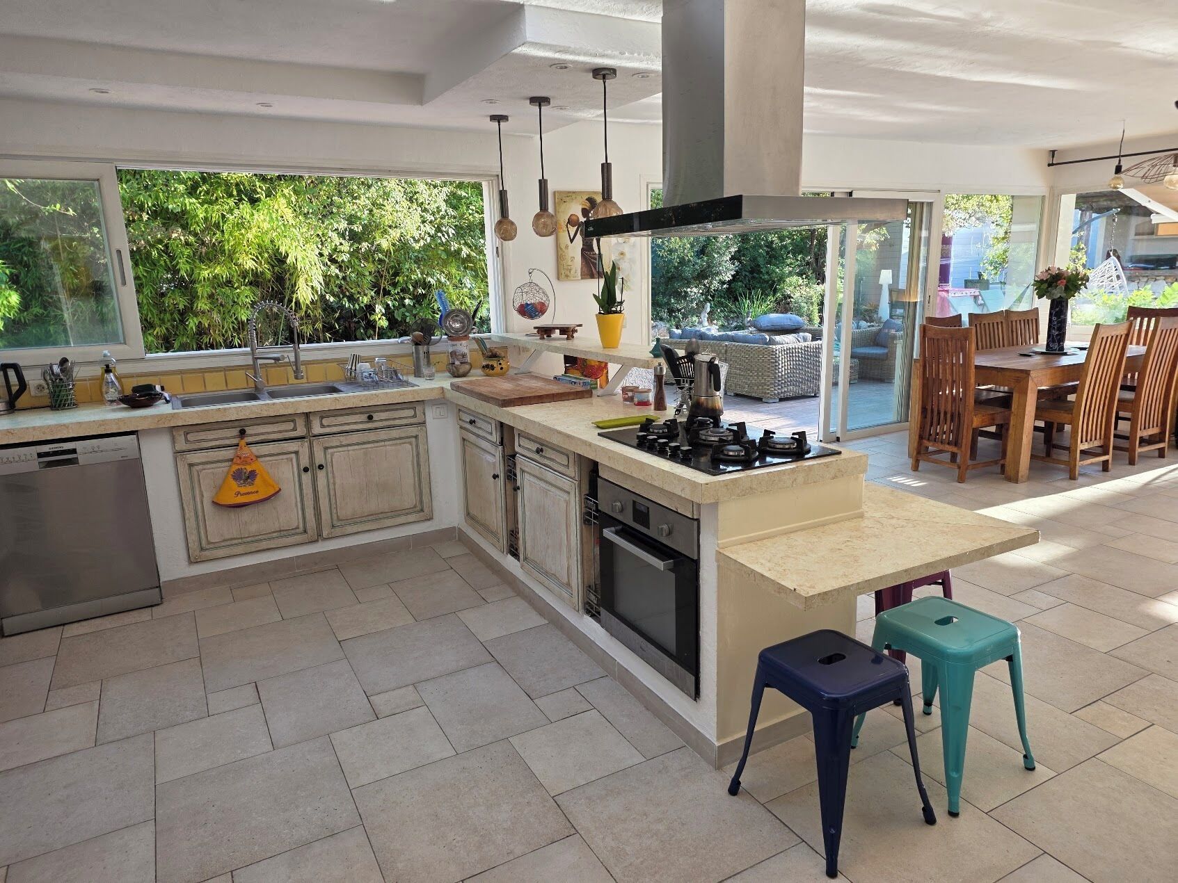 Une cuisine moderne dotée d’un îlot central, d’appareils électroménagers intégrés et d’un coin repas avec espace extérieur.