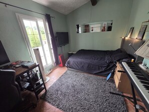 A bedroom with a bed, a desk with a computer, a keyboard, a TV, and a window with curtains. - A tropical getaway in a private villa near the sea and Nice on the French Riviera! (La Gaude)