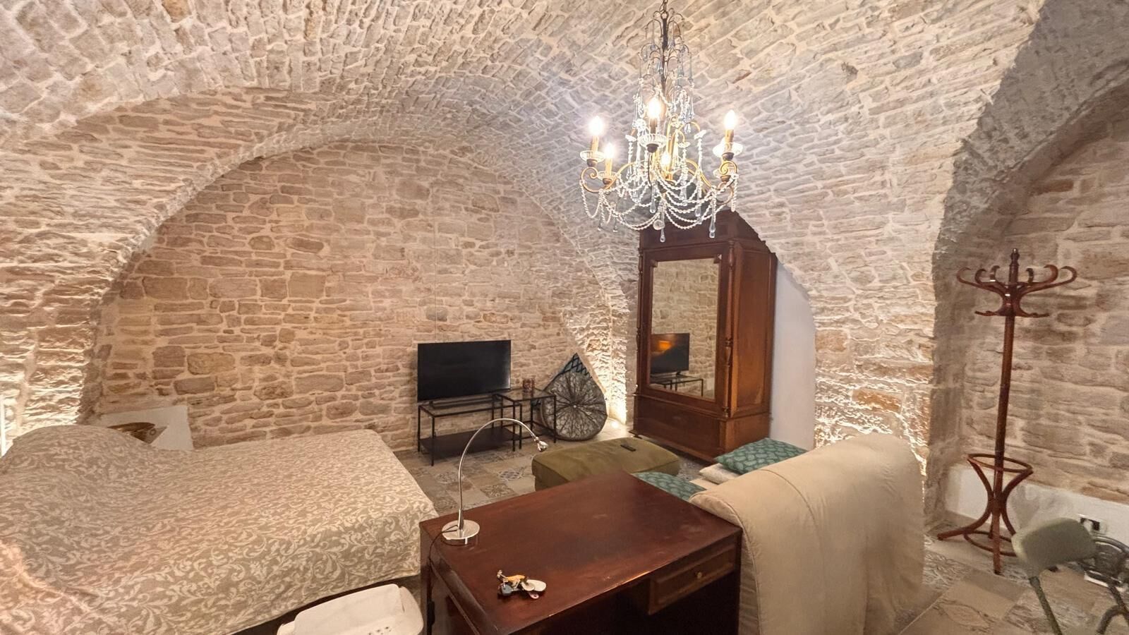 Ein Zimmer mit Stehwänden, einer Kristallleuchter, einem Bett, einem Sofa, einem Tisch, einem Fernseher und einem Kleiderständer.