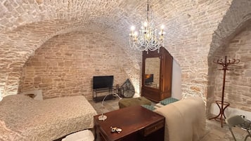 Ein Zimmer mit Stehwänden, einer Kristallleuchter, einem Bett, einem Sofa, einem Tisch, einem Fernseher und einem Kleiderständer.