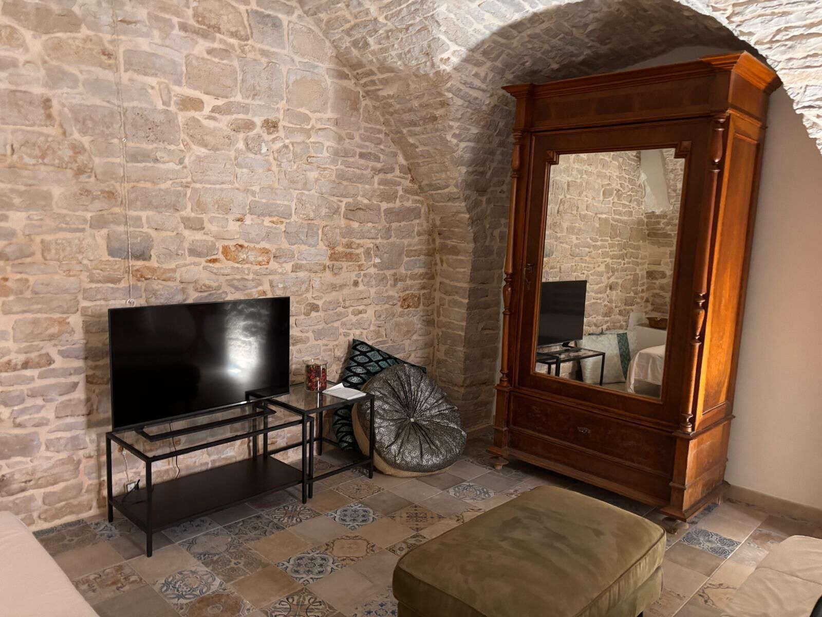 A stone-walled room with a television on a stand, a wooden cabinet, and a patterned floor.