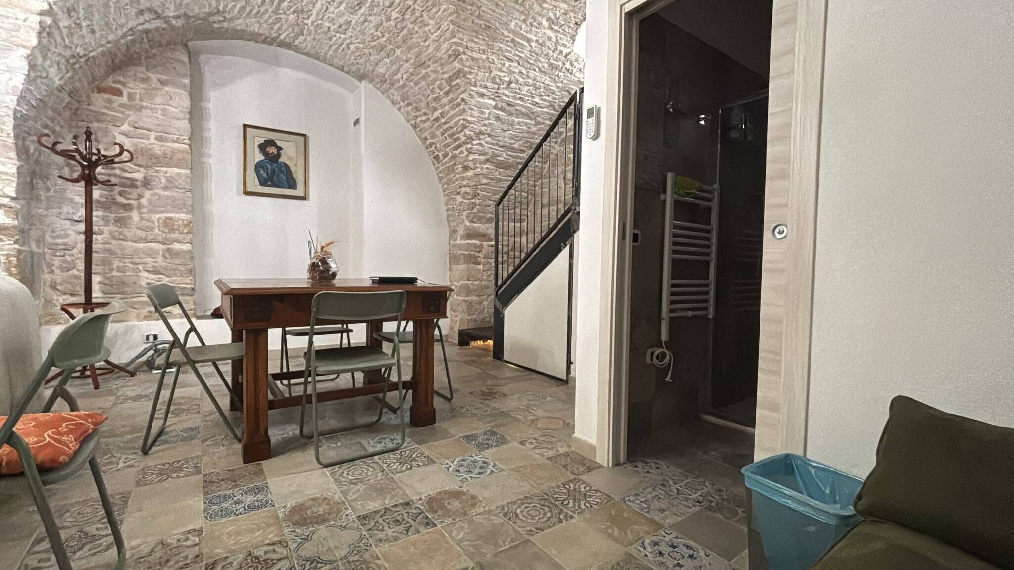 A dining area with a stone wall, a staircase, and a view of a room with a bed.