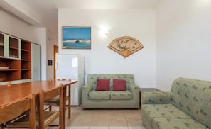 A living room with a wooden dining table, a green sofa, and a small refrigerator.