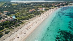 An aerial view of a coastal area with houses along the beach, clear turquoise waters, and a distant bridge.
