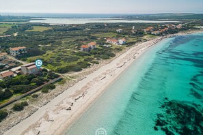 An aerial view of a coastal area with houses along the beach, clear turquoise waters, and a distant bridge.