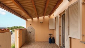 A covered outdoor area with a shower, two gas cylinders, and a door leading to a building.
