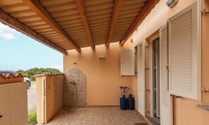 A covered outdoor area with a shower, two gas cylinders, and a door leading to a building.