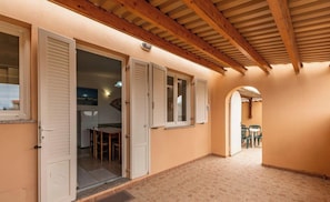 A corridor with wooden beams, a tiled floor, and a view into a room with a table and chairs.