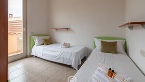 A hotel room with two single beds, a small window, and a door leading to an outdoor area.
