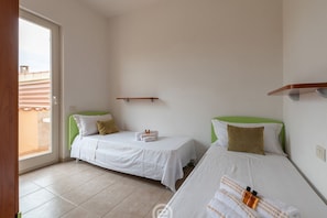 A hotel room with two single beds, a small window, and a door leading to an outdoor area.