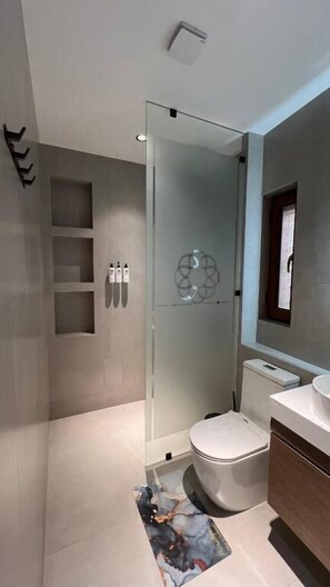 Een moderne badkamer met een glazen douchecabine, toilet en een wastafel met spiegel.