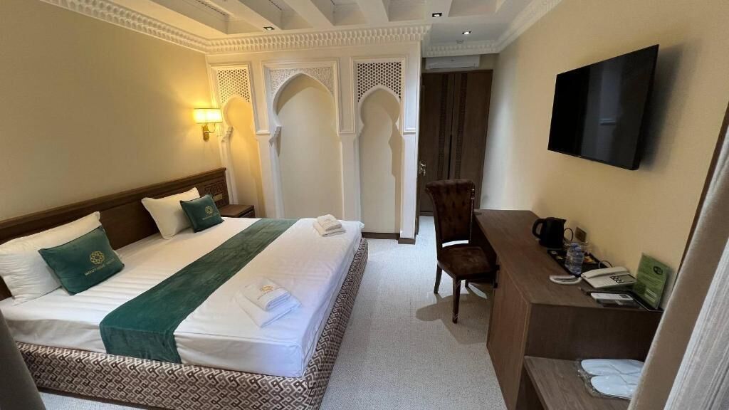 A hotel room with a bed, a desk, a chair, a television, and a decorative wall.