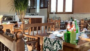 A spacious living area with wooden furniture, a large window, and a kitchen in the background. - Shams Boutique Hotel (Bukhara)