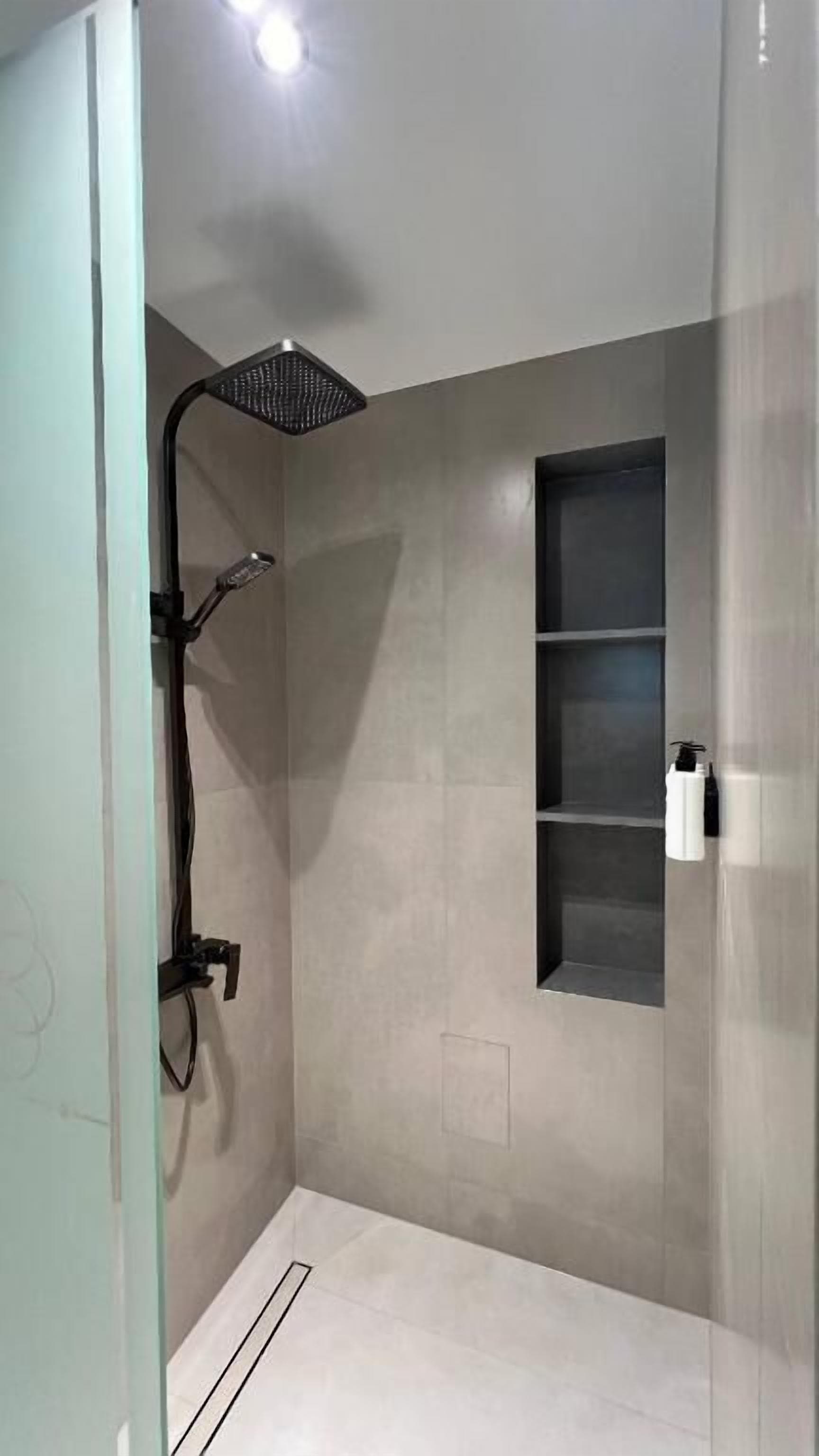 Um chuveiro moderno com um chuveiro manual, prateleira embutida e porta de vidro.