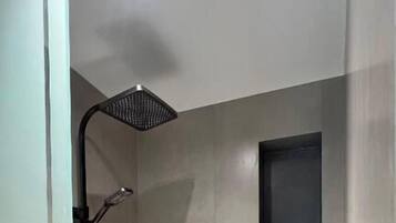 Um chuveiro moderno com um chuveiro manual, prateleira embutida e porta de vidro.