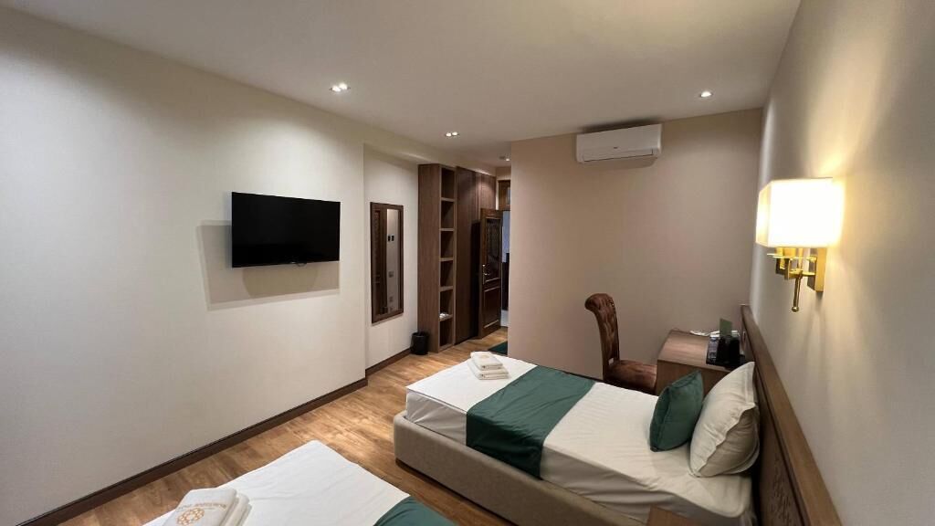 Habitació d'hotel amb dos llits, un televisor fixat a la paret, una cadira, una taula de nit i una làmpada.