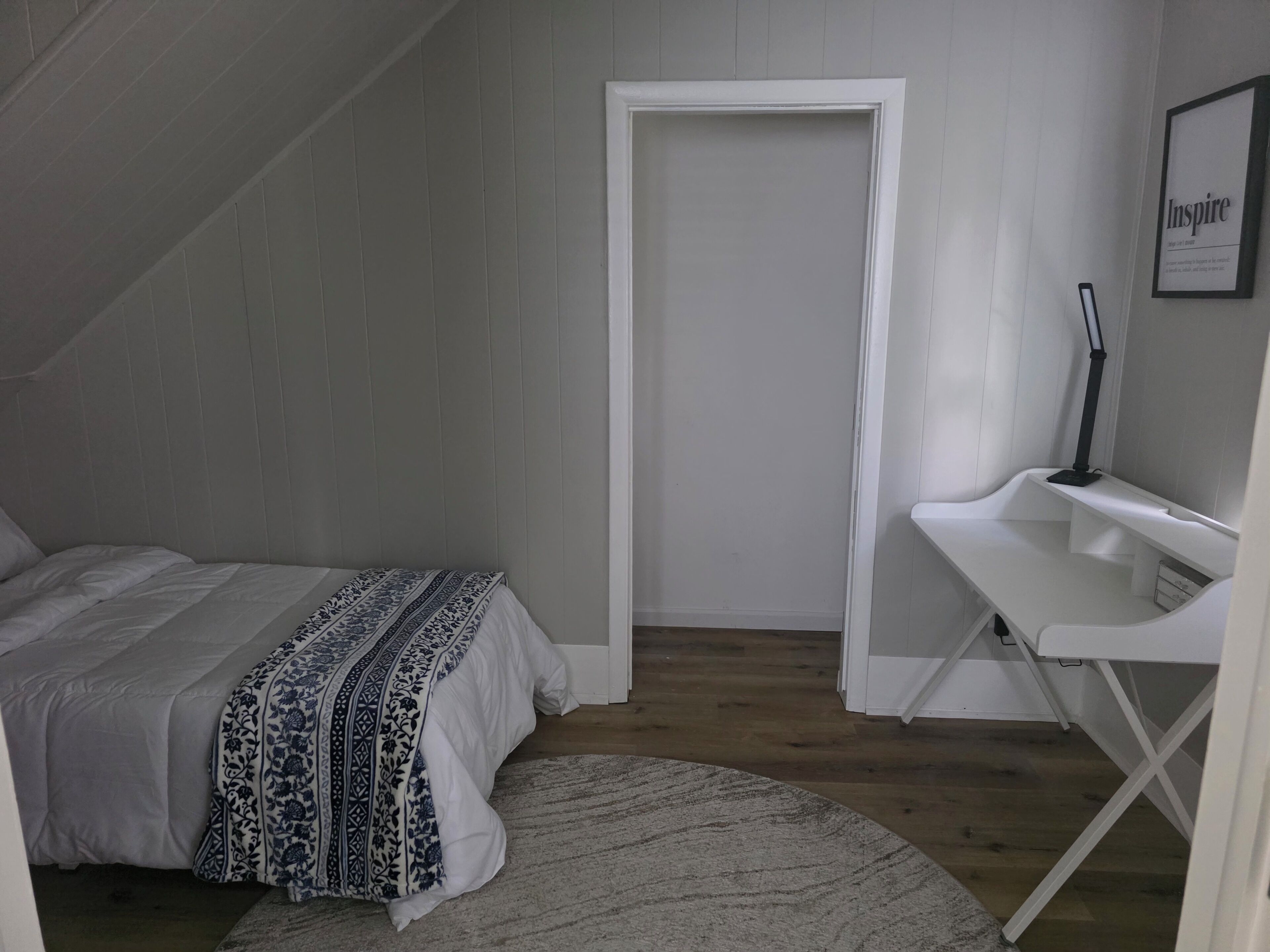A bedroom with a bed, a desk, and a door.
