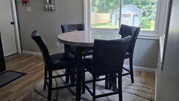 A dining area with a round table and chairs, a large window with a view of the outdoors, and a fire extinguisher on the wall.