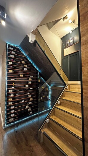 A staircase with a wine rack on the left and a wall-mounted light fixture above. - Modern Home in Surrey Quays/ Canada Water (London)