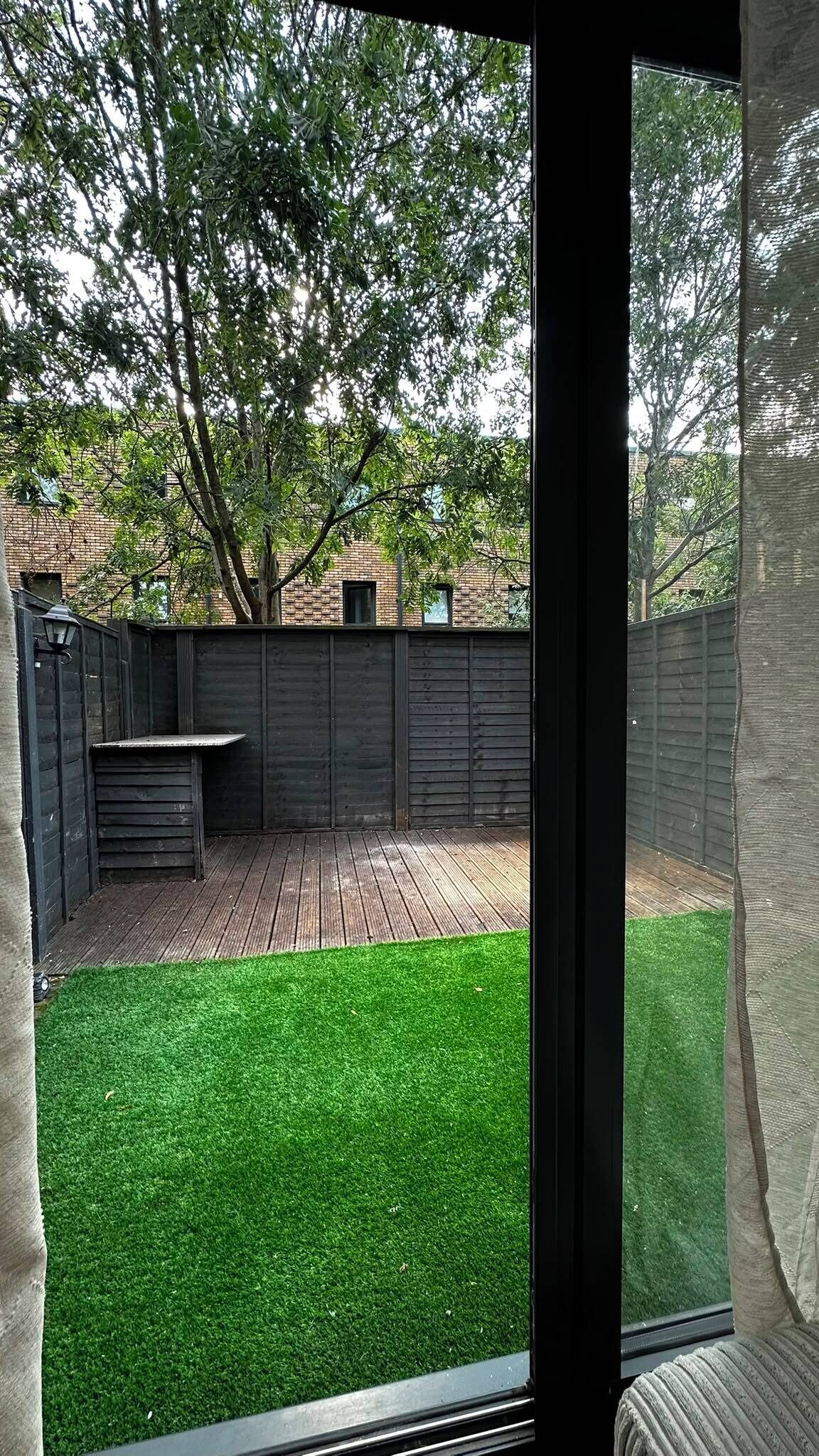 Blick auf einen Garten mit einer Holzterrasse, einem Rasen und einer Backsteinmauer.