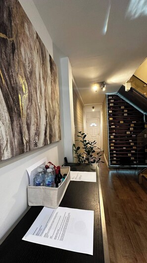 A hotel reception area with a marble wall, a wooden staircase, and a reception desk with a bottle holder and papers. - Modern Home in Surrey Quays/ Canada Water (London)