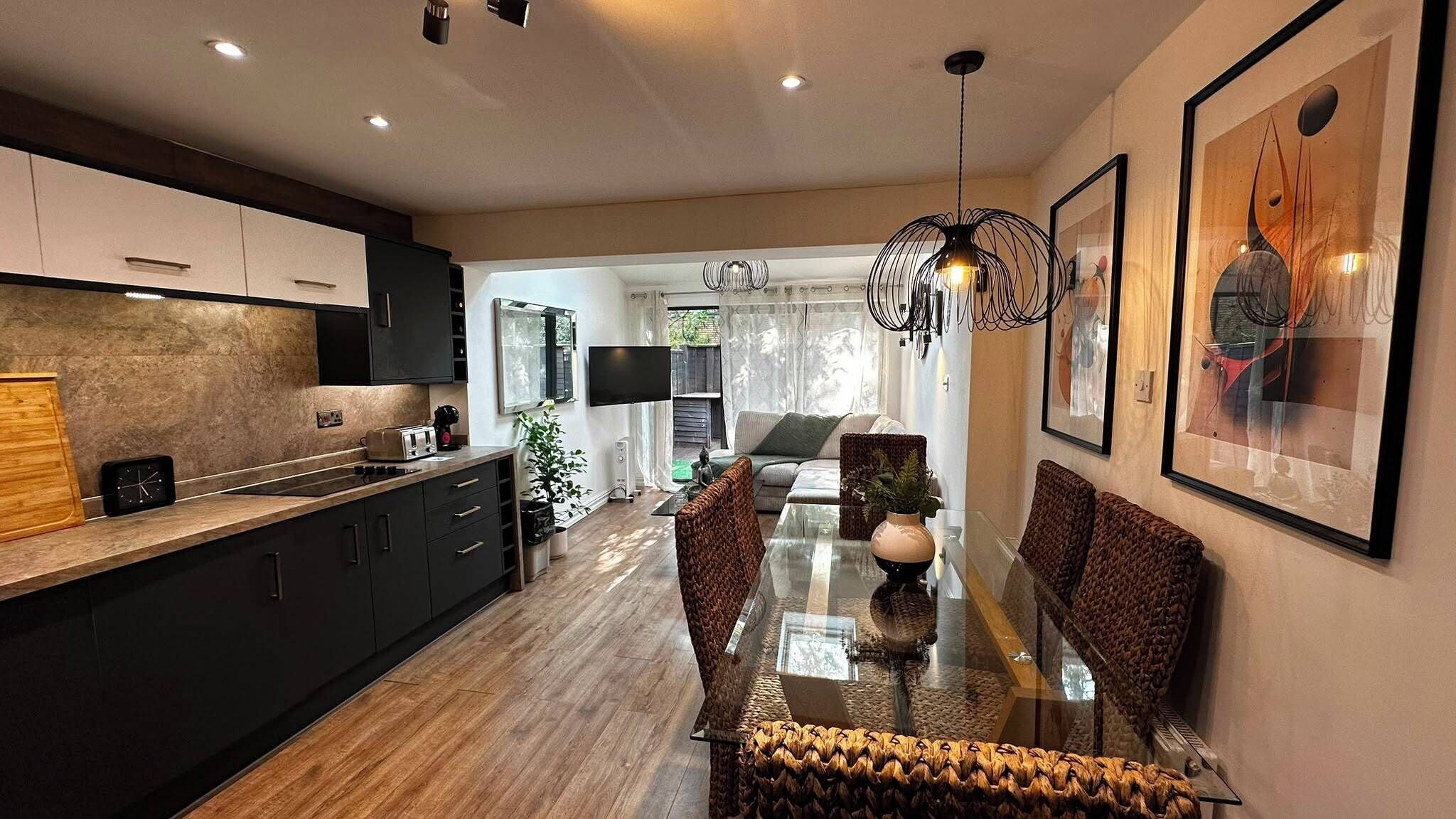 A modern kitchen with dark cabinets, a wooden countertop, and a dining area with a glass table and woven chairs.