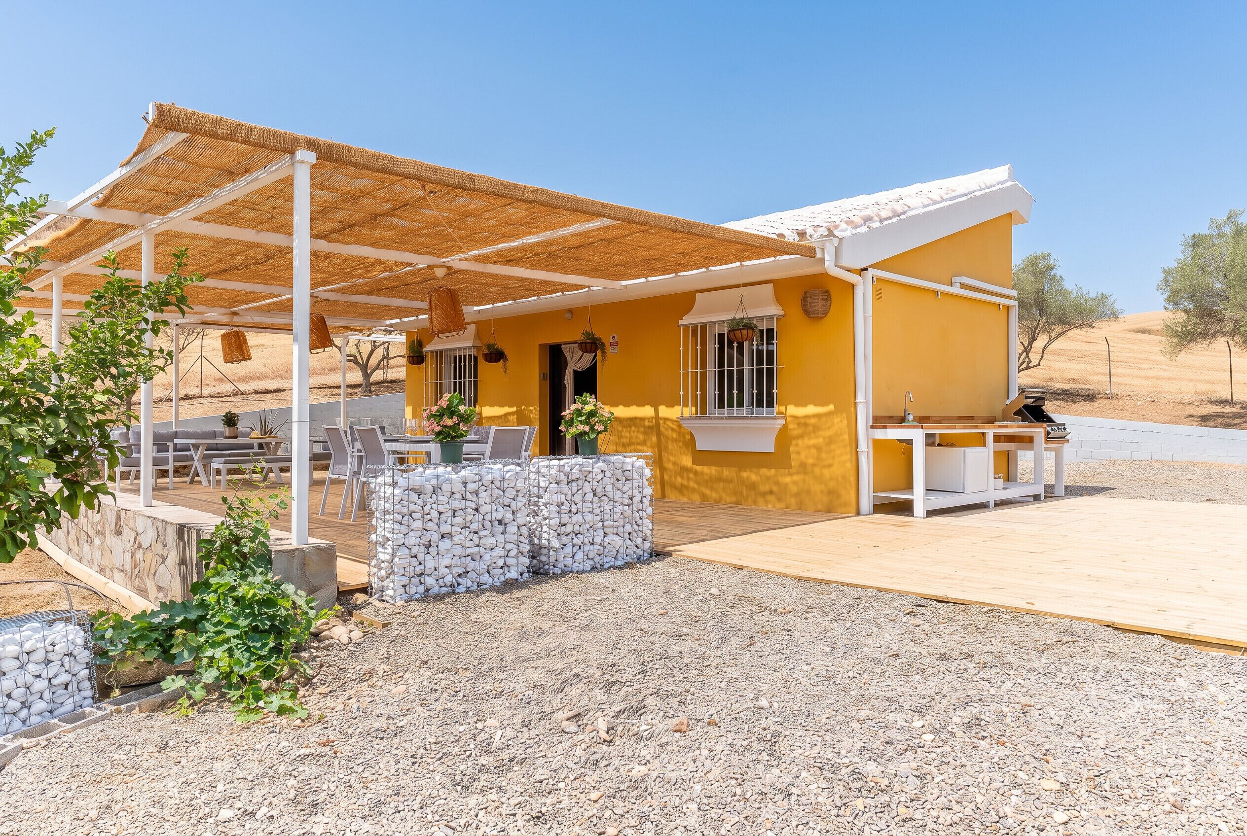 Ein gelbes Gebäude mit überdachter Terrasse, Außenplätzen und Kiesgrundstück.