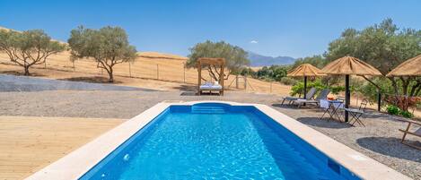A rectangular swimming pool with clear blue water, surrounded by a wooden deck and a pebble ground.