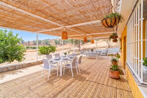 Eine Terrasse im Freien mit Esstisch und Stühlen, umgeben von einer hängenden Pflanze.