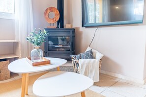 A cozy living room with a fireplace, a round table, a wicker chair, and a large window. - Cubo's Casa Alaya & Oasis Pool / Private pool / Air conditioning / BBQ / Free Wi-Fi (Coín)