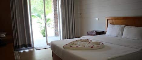 A hotel room with a bed, a nightstand, a wooden headboard, and a view through a glass door to the outside.