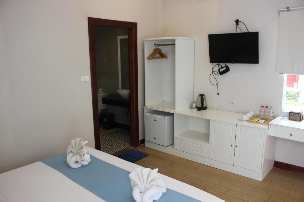A hotel room with a bed, a wardrobe, a desk, a television, and a bathroom visible through an open door.